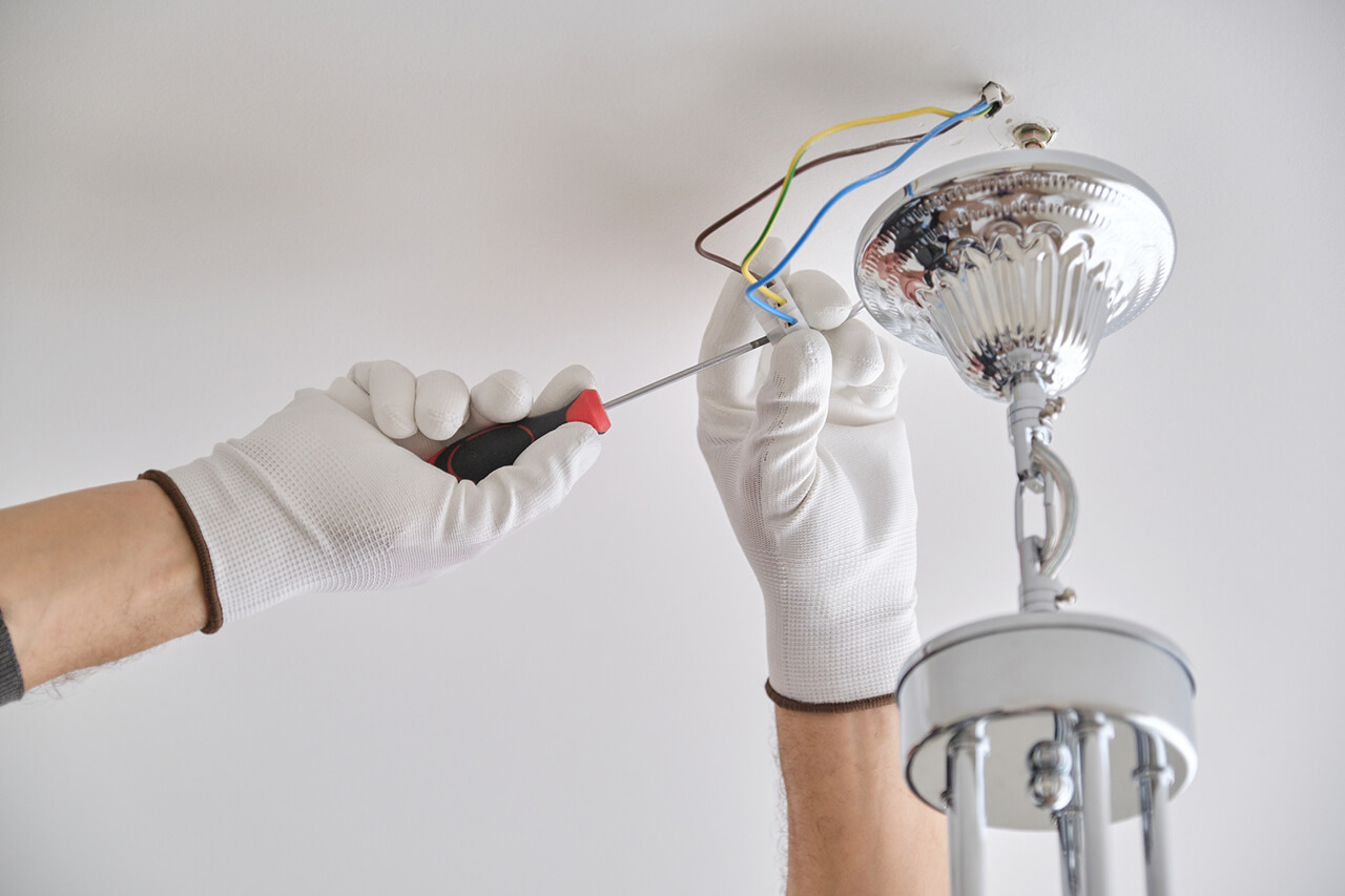 electrician repairing lighting fixture on the ceiling of home