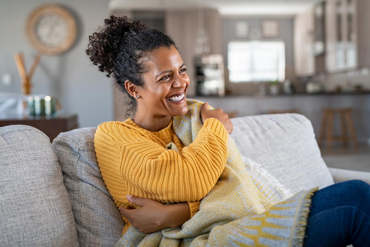 A woman covered in a blanket laughing while sitting on the sofa